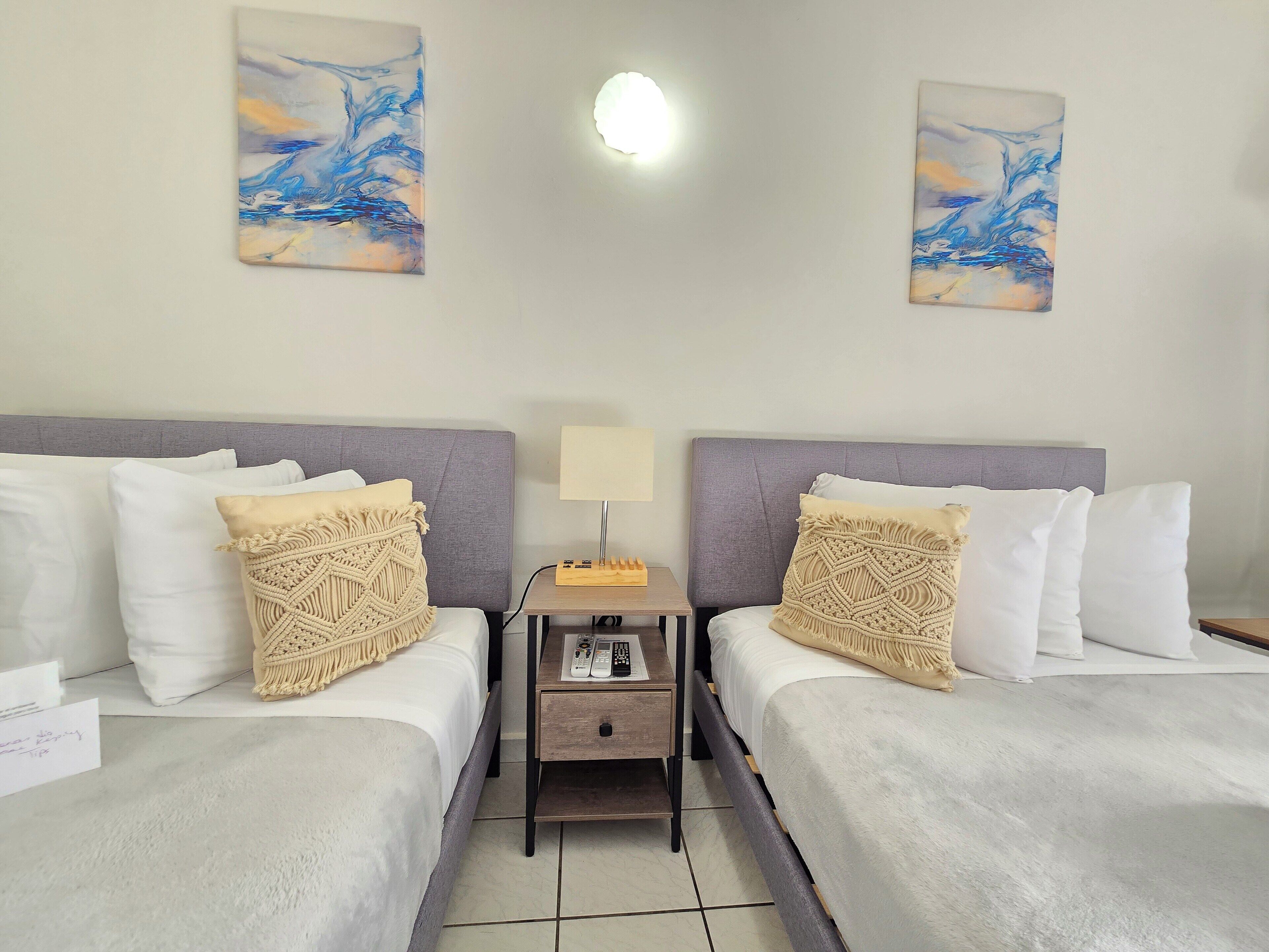 Een hotelkamer met twee bedden, een nachtkastje met een lamp, en twee abstracte schilderijen aan de muren.