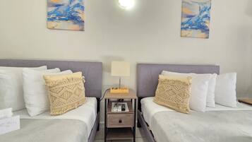 Een hotelkamer met twee bedden, een nachtkastje met een lamp, en twee abstracte schilderijen aan de muren.