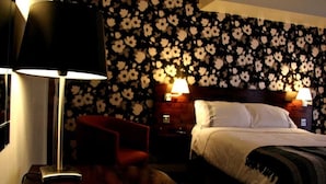 A hotel room with a bed, two bedside lamps, a red chair, and a wooden floor. - Hotel Belmonte (Norwich)