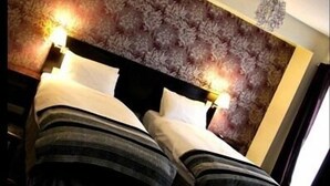 A hotel room with a patterned headboard, two beds with striped bedding, and a chandelier. - Hotel Belmonte (Norwich)