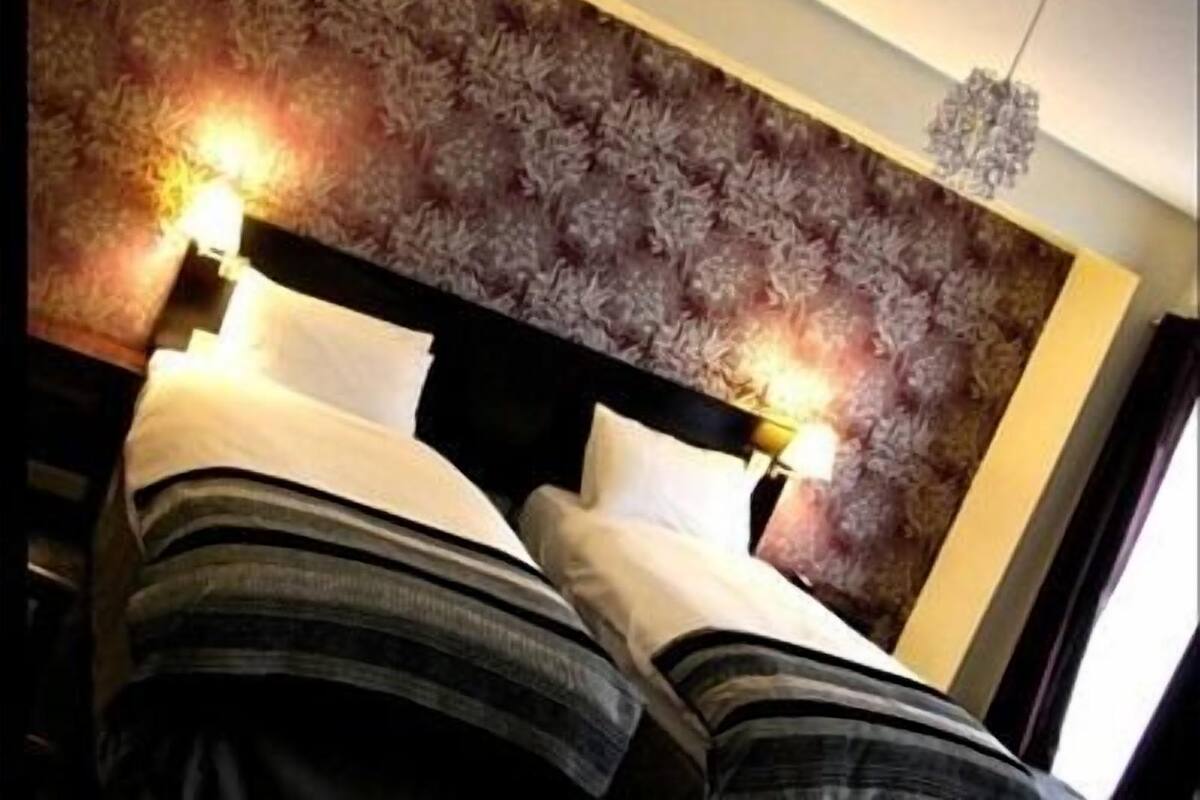 A hotel room with a patterned headboard, two beds with striped bedding, and a chandelier.