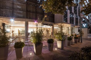 An outdoor cafe area with tables and chairs, surrounded by large planters with greenery. - Vivaldi Hotel Loft Punta Carretas (Montevideo)