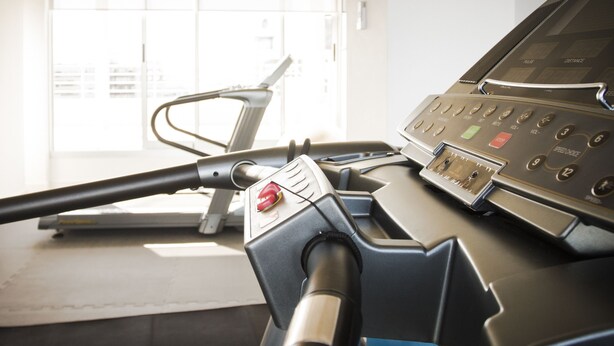 A treadmill with a control panel, a window with blinds, and a city view.