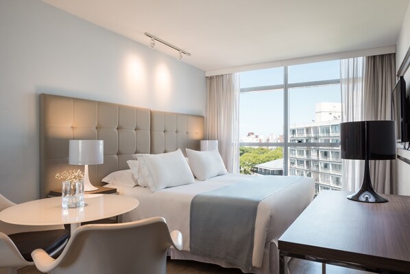 A hotel room with a large bed, a round table, and a view of the city. - Vivaldi Hotel Loft Punta Carretas (Montevideo)