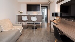A modern living room with a sofa, a wooden dining table, two white bar stools, and a kitchen area in the background. - Vivaldi Hotel Loft Punta Carretas (Montevideo)