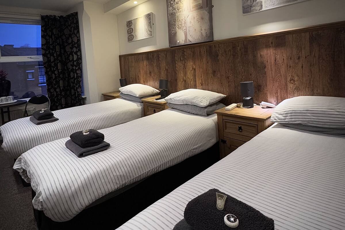 Une chambre d’hôtel avec deux lits simples, une tête de lit en bois, des tables de chevet avec des lampes et des œuvres d’art accrochées aux murs.