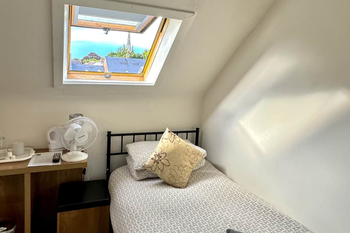 Une petite pièce bien éclairée, équipée d’un lit, d’un bureau et d’une fenêtre donnant sur un paysage pittoresque.