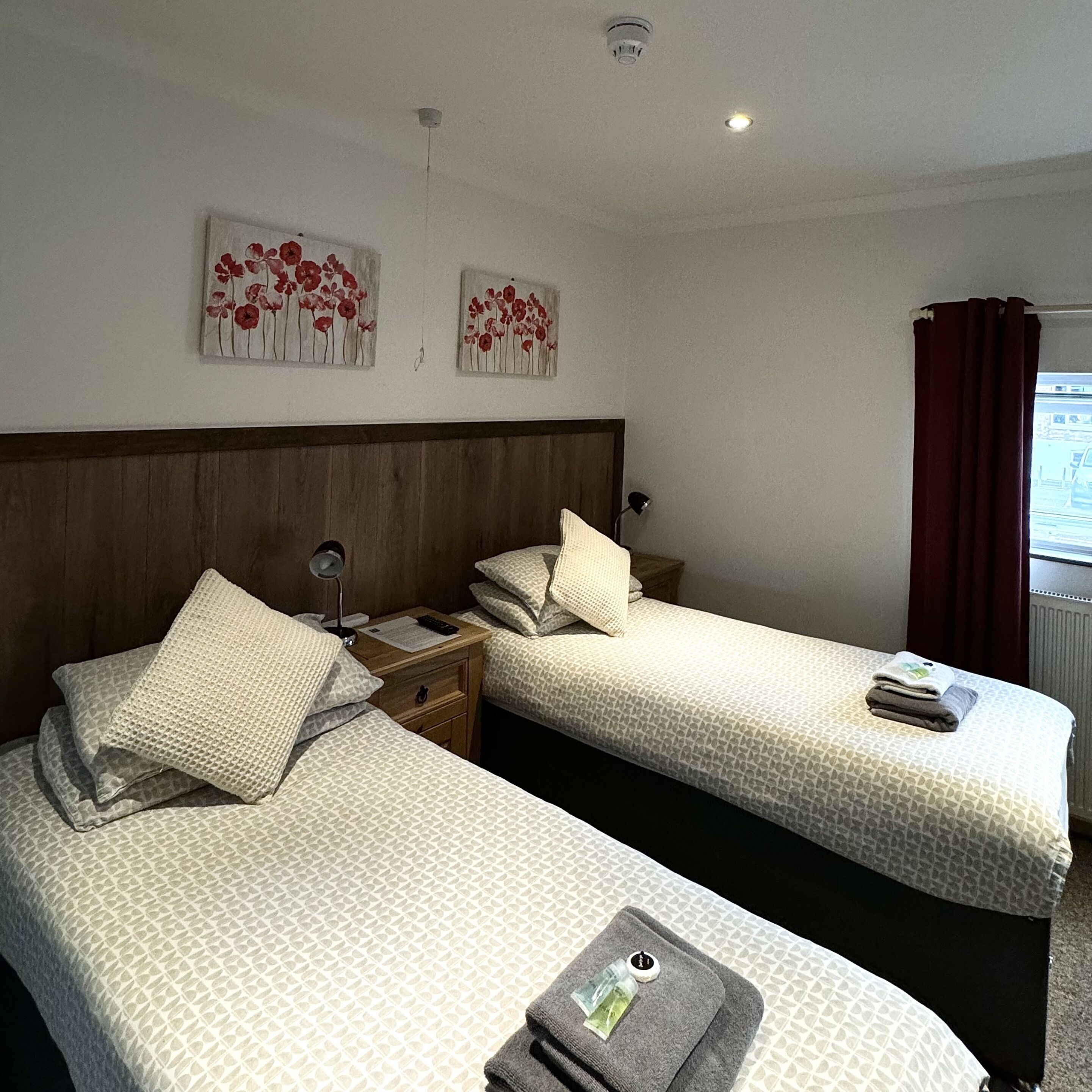 Quarto de hotel com duas camas, cabeceira de madeira e dois quadros de flores pendurados na parede.