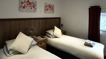 Quarto de hotel com duas camas, cabeceira de madeira e dois quadros de flores pendurados na parede.
