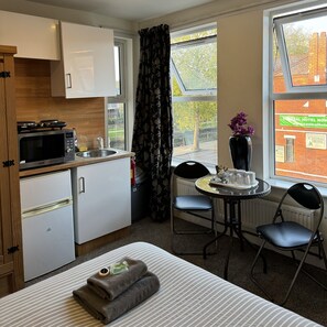 A compact hotel room with a kitchenette, a dining area, and a bed.