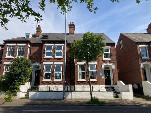 A row of red brick terraced houses with white window frames and a central tree.