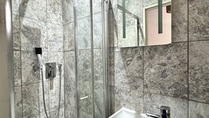 Une salle de bain moderne avec une douche en verre, un lavabo blanc et un mur recouvert de carreaux de marbre.