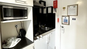 Une petite cuisine équipée d’un four à micro-ondes, d’une cuisinière et d’un évier. On y trouve des placards, un plan de travail et une porte signalée comme issue de secours.