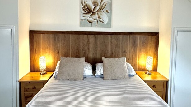 Une chambre d’hôtel avec un grand lit, deux tables de chevet avec des lampes, une tête de lit en bois et une œuvre d’art florale au-dessus du lit.