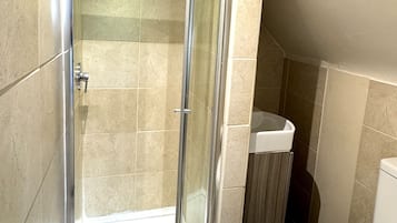 A shower with a glass door, a toilet, and a sink in a bathroom with tiled walls and wooden flooring.