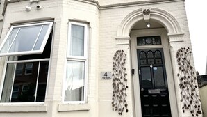 Un bâtiment à deux étages avec une porte d’entrée noire, une plaque portant le numéro « 4 » et des motifs de feuilles décoratives sur les murs.