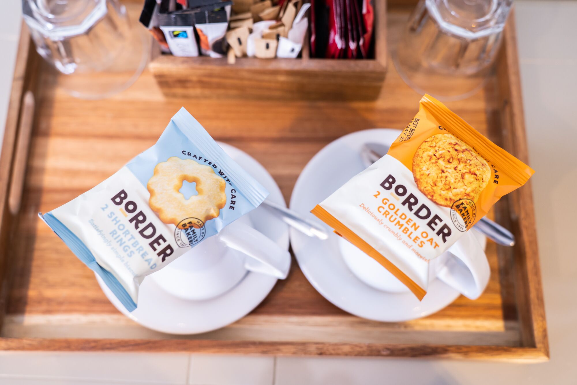 A tray with two plates, one holding a packet of Border shortbread and the other holding a packet of Border golden oat crumbles.