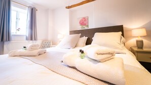 Une chambre d’hôtel avec un grand lit, des serviettes soigneusement pliées, une table de chevet avec une lampe et une fenêtre avec des rideaux.