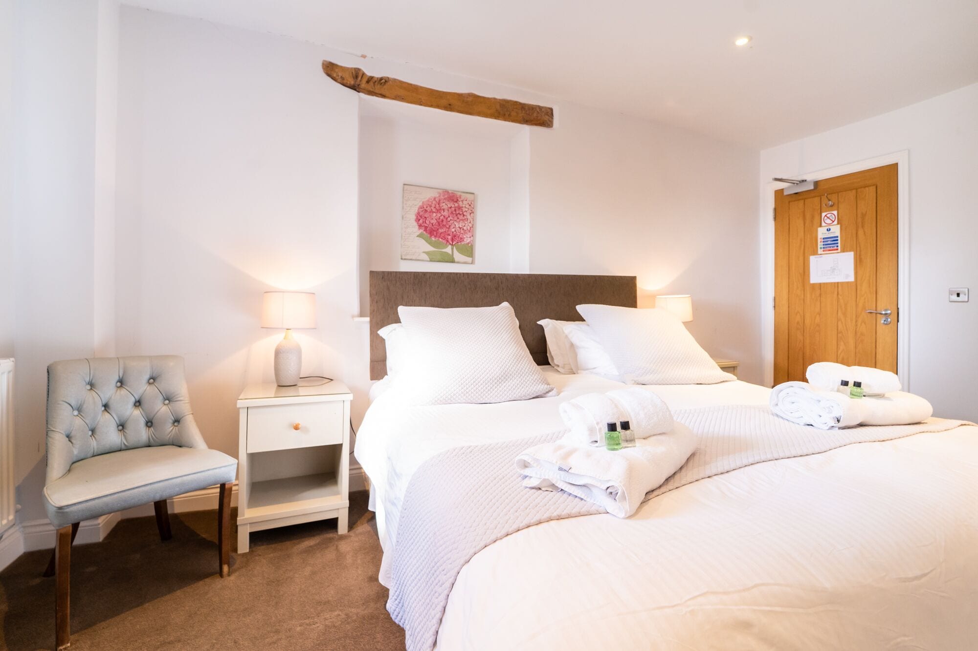 A hotel room with a bed, two bedside tables, a chair, and a wooden headboard.