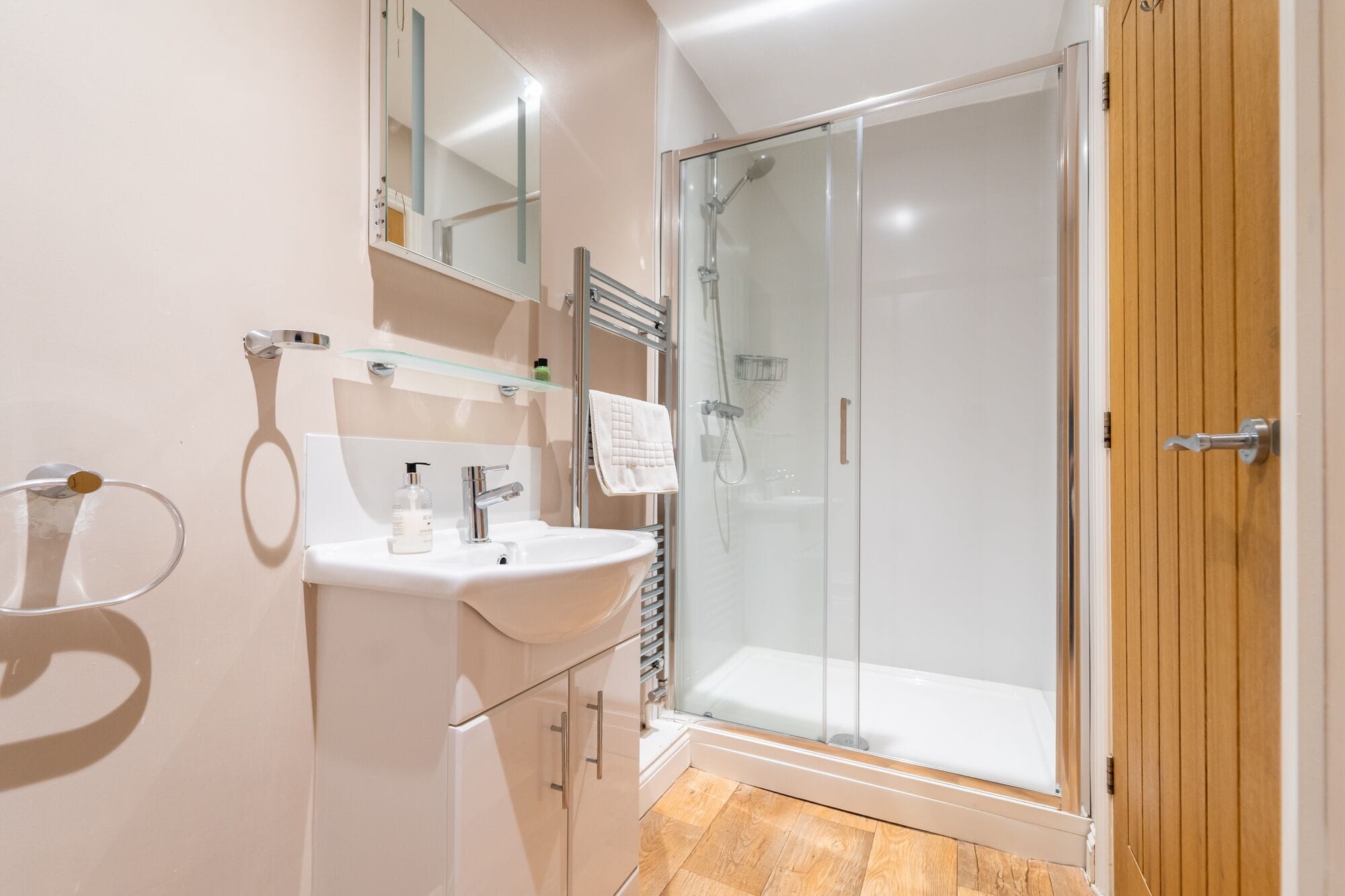 A modern bathroom with a glass shower enclosure, a white sink, and a wooden door.