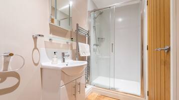 A modern bathroom with a glass shower enclosure, a white sink, and a wooden door.