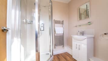 Un baño moderno con cabina de ducha de vidrio, un lavabo blanco con espejo y suelo de madera.