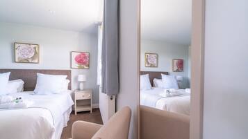 A hotel room with two beds, a bedside table with a lamp, and floral artwork on the walls.