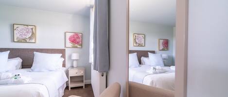 Een hotelkamer met twee bedden, een nachtkastje met een lamp, en bloemistische kunst aan de muren.