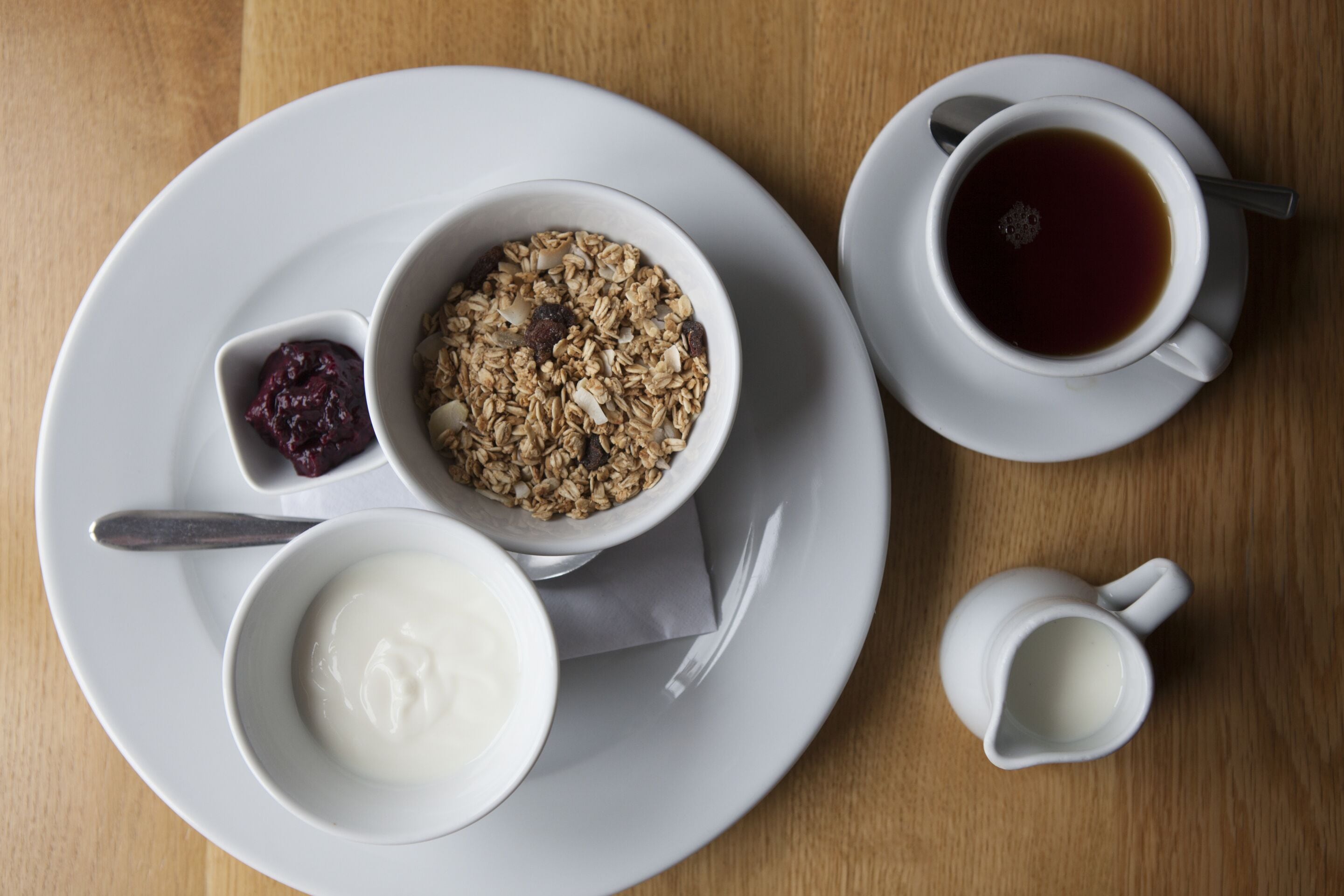 Ein Frühstückstisch mit Granola, Joghurt und einer Tasse Tee.