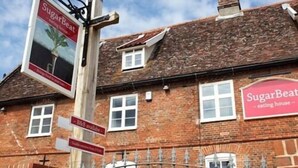 Un bâtiment en briques sur lequel on peut lire l’inscription « SugarBeat eating house », ainsi qu’un panneau indiquant « Chambres d’hôtes disponibles » et « Produits locaux de la ferme ».