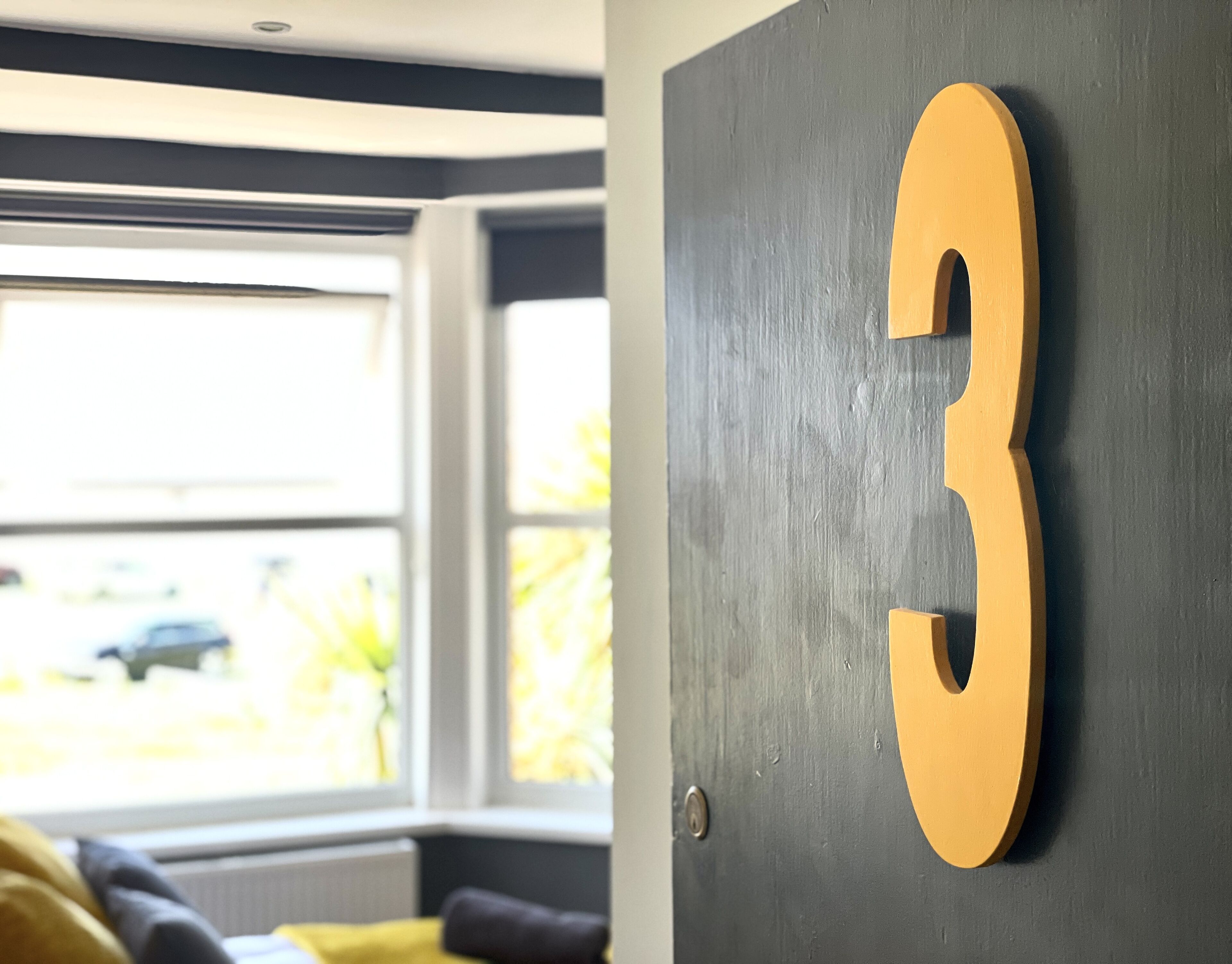 A room with a large window, a dark gray wall, and a wooden number '3' decoration.