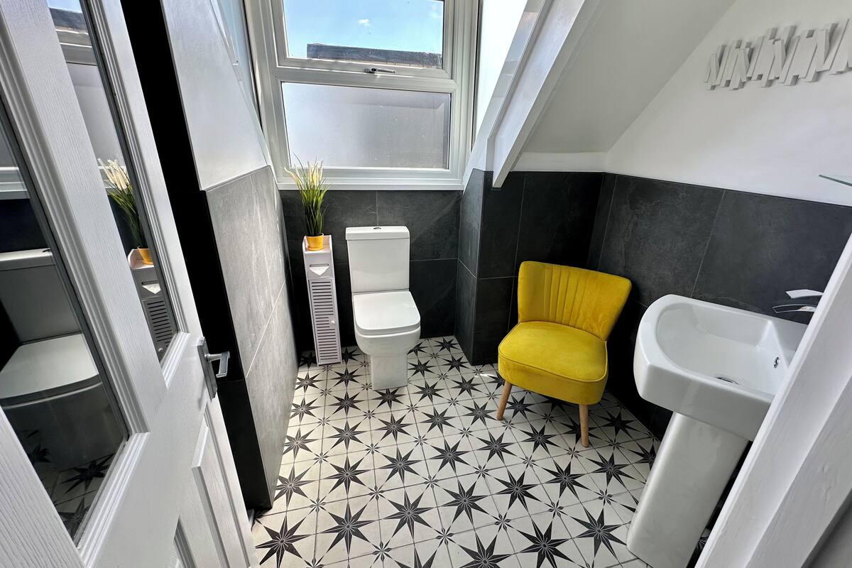 Une salle de bain avec un carrelage au motif étoilé, une chaise jaune, un lavabo blanc et des toilettes.