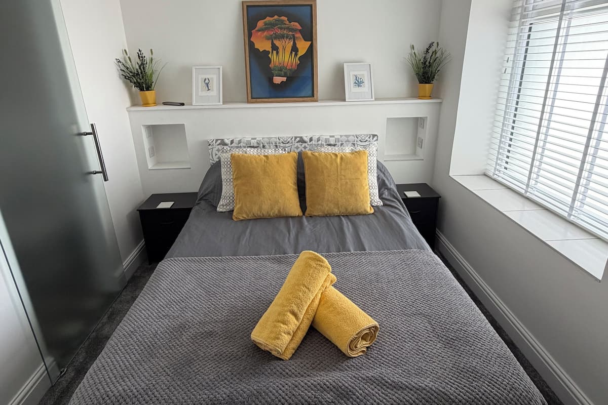 Une chambre à coucher avec un lit, un tableau, une fenêtre avec des stores et une porte.