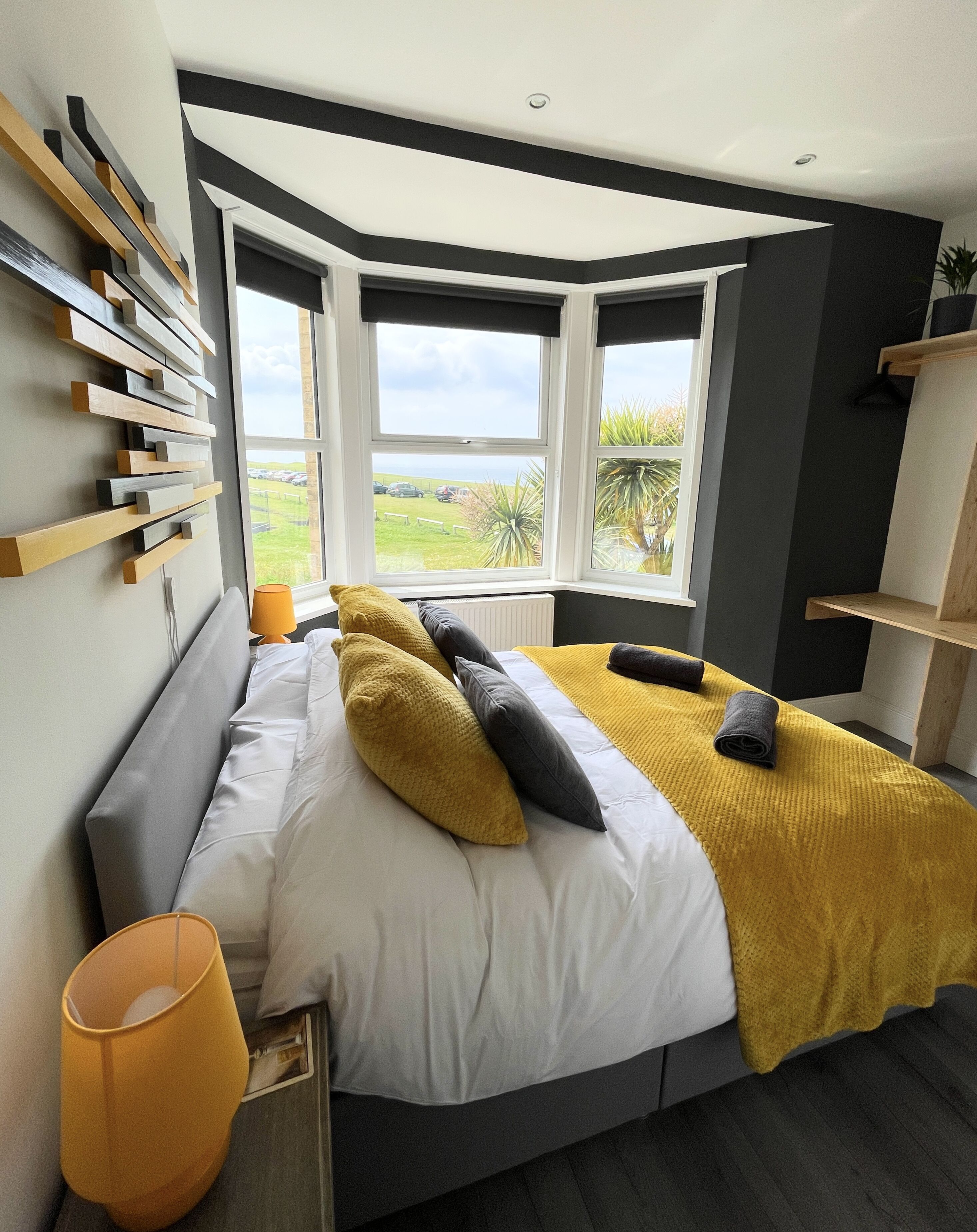 A modern bedroom with a large bed, a view of the outdoors, and a unique wall design.