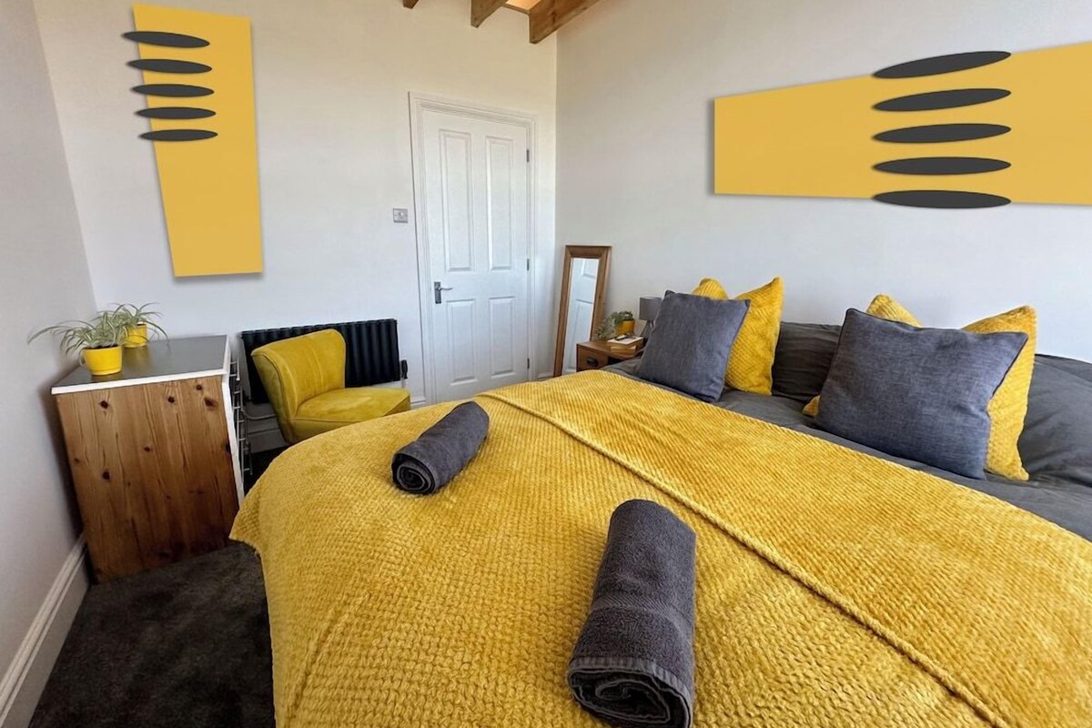 Un dormitorio con cama, mesita de noche, silla, puerta y pared con arte abstracto.