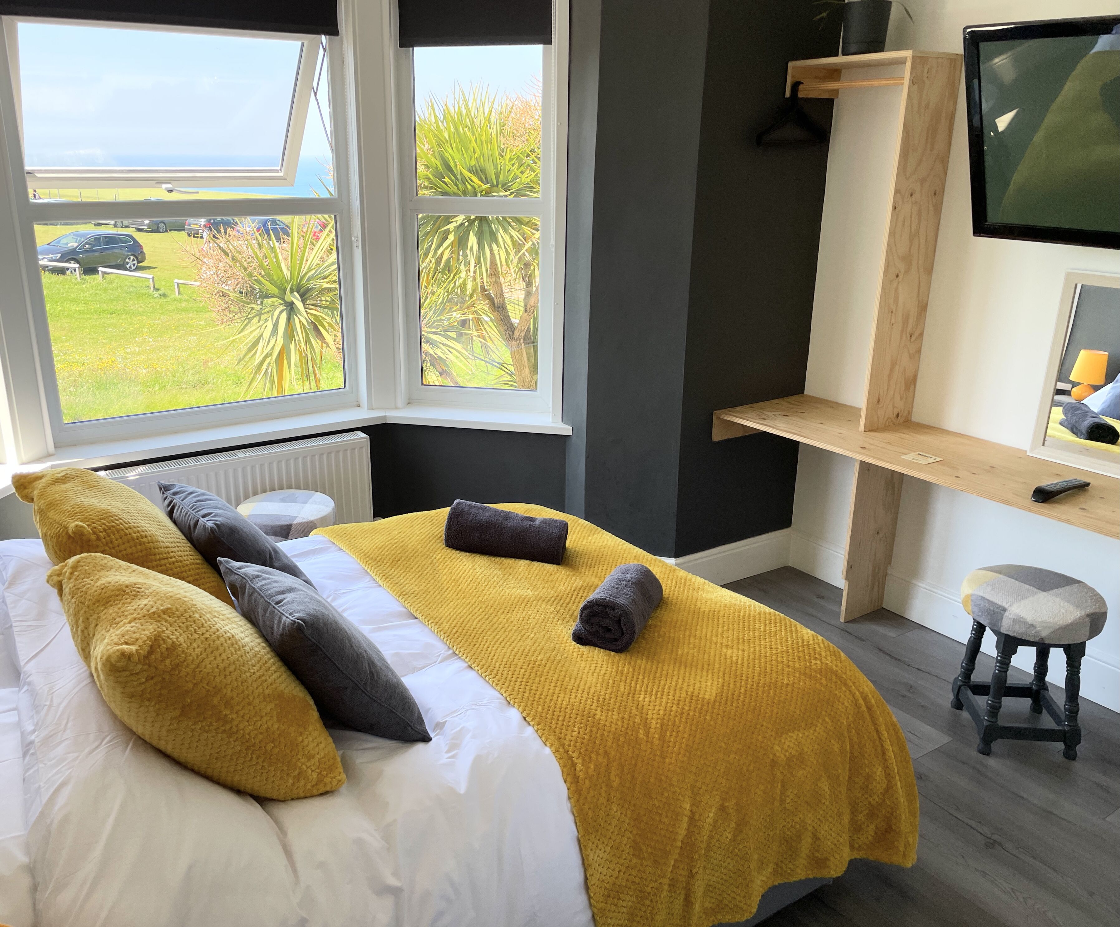 A bedroom with a bed, a window, a TV, and a small stool.