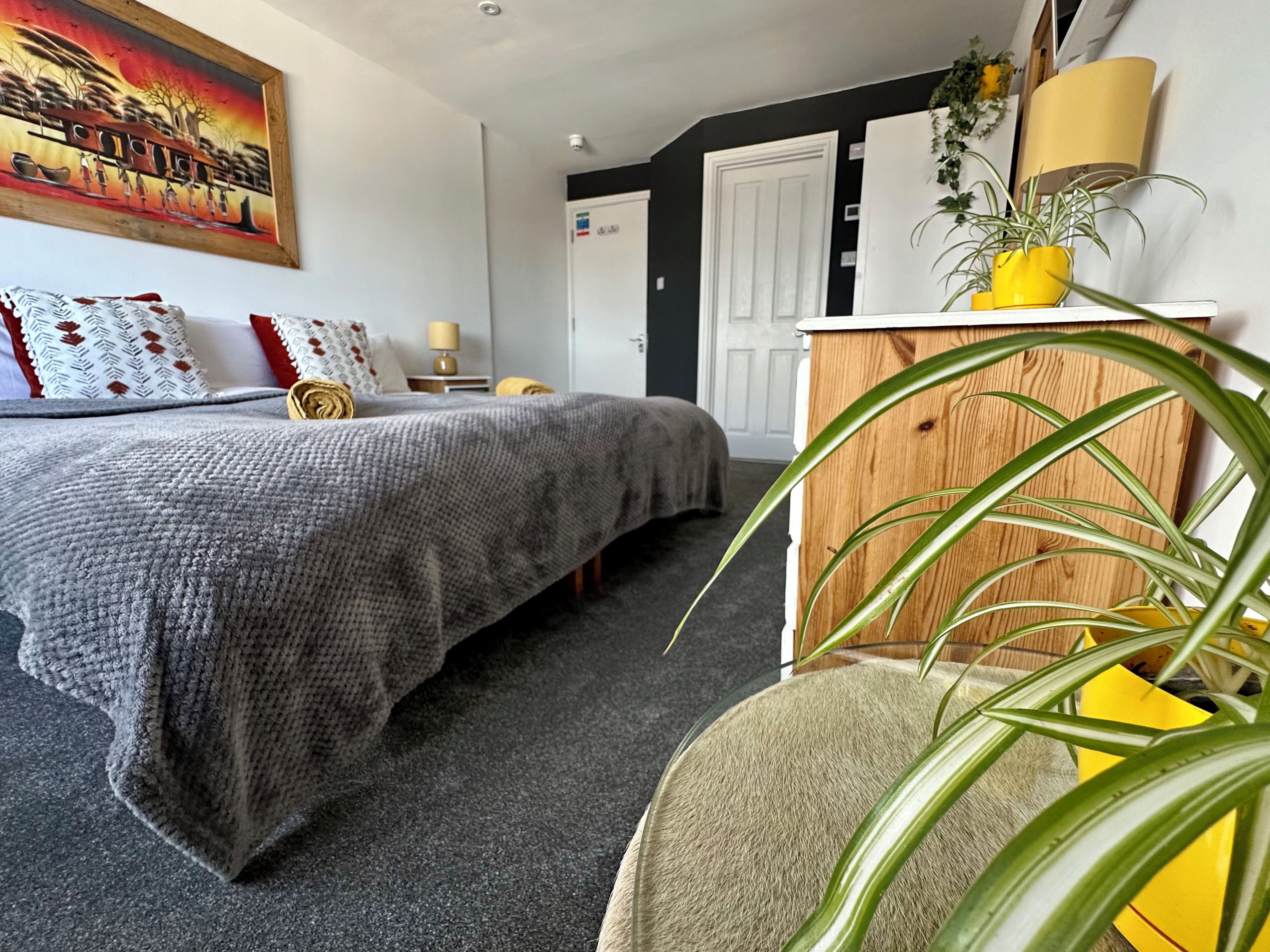 Un dormitorio con cama, mesita de noche, lámpara, cómoda y un cuadro en la pared.
