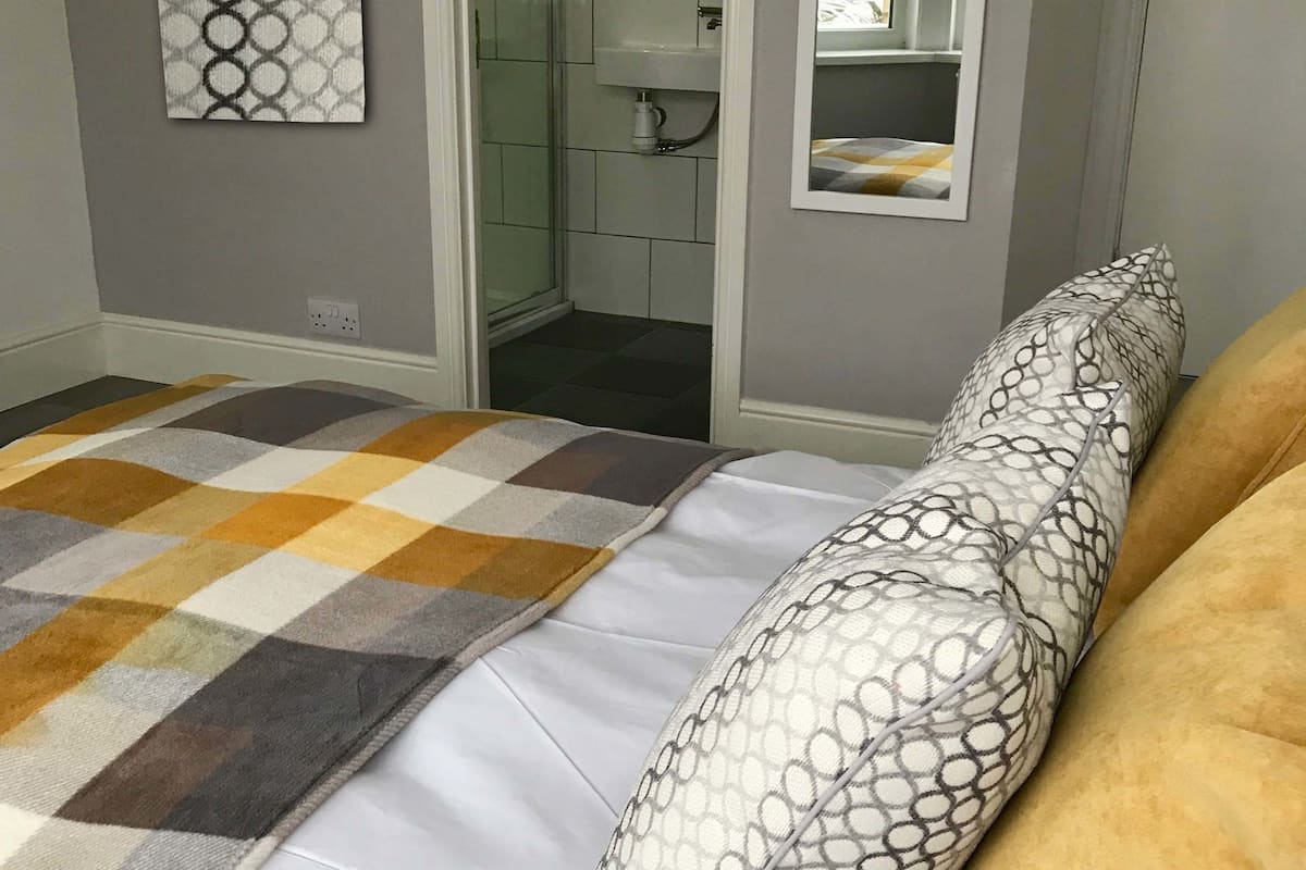 Une chambre avec une couvre-lit à carreaux, un coussin à motifs et un miroir au-dessus de la porte.
