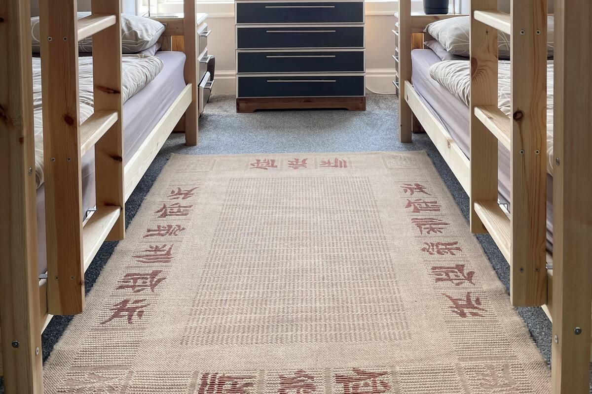 Une chambre avec des lits superposés, une commode, une fenêtre et un tapis.