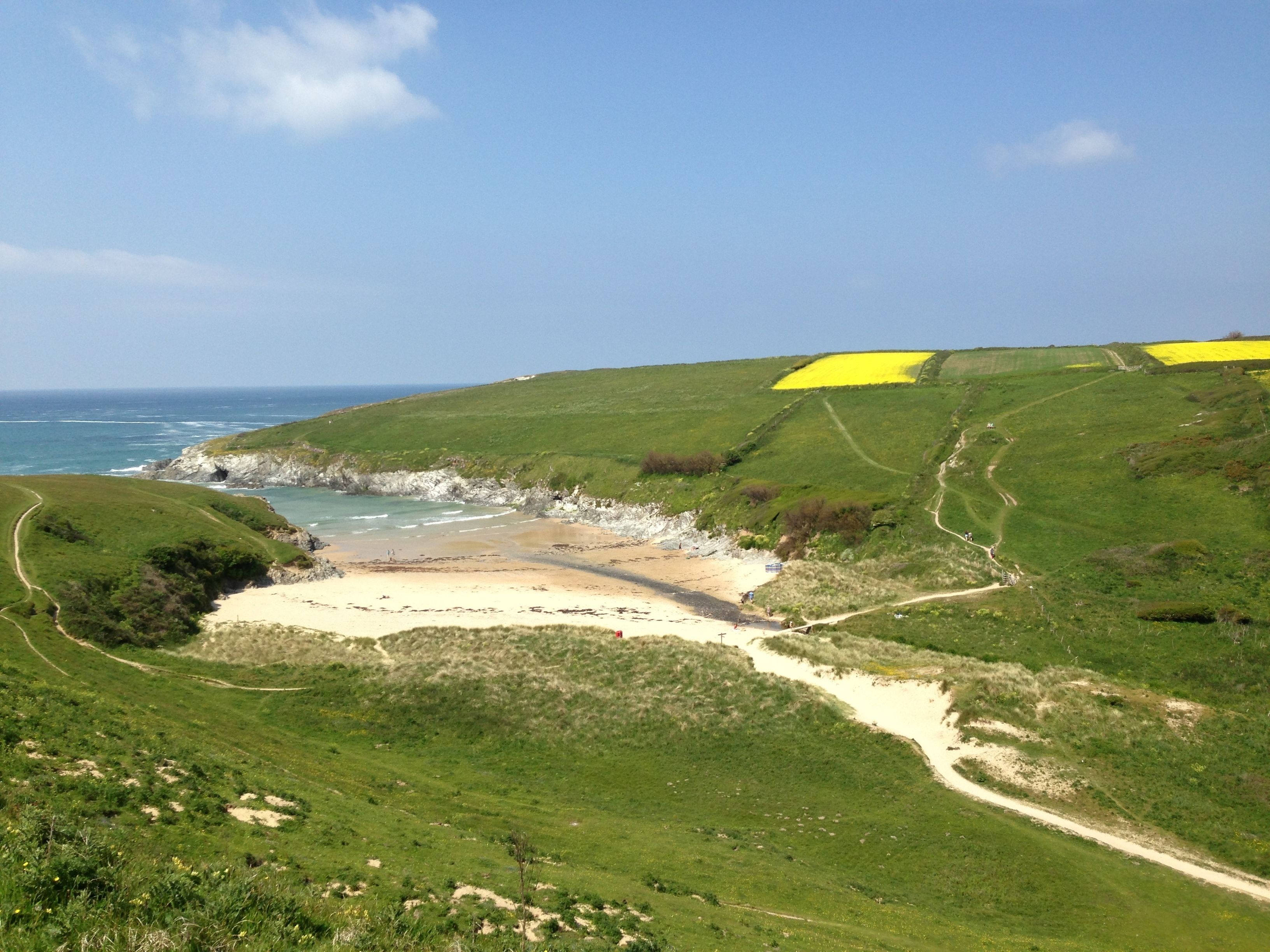A coastal landscape with a sandy beach, grassy hills, and a clear blue sky.