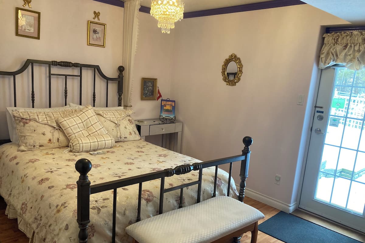 Een slaapkamer met een bed, een bankje, een nachtkastje, een kroonluchter en een deur met uitzicht.