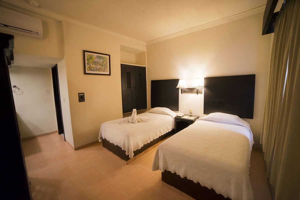 A hotel room with two beds, a nightstand, a lamp, and a painting on the wall.