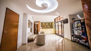 Um saguão de hotel com luminária em espiral no teto, balcão de recepção, máquina de vendas automáticas e área de estar.