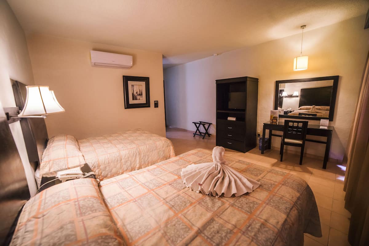 A hotel room with two beds, a desk, a chair, a television, and an air conditioning unit.