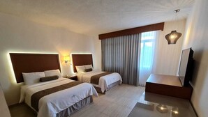 Quarto de hotel com duas camas, uma escrivaninha, televisão e janela com cortinas.