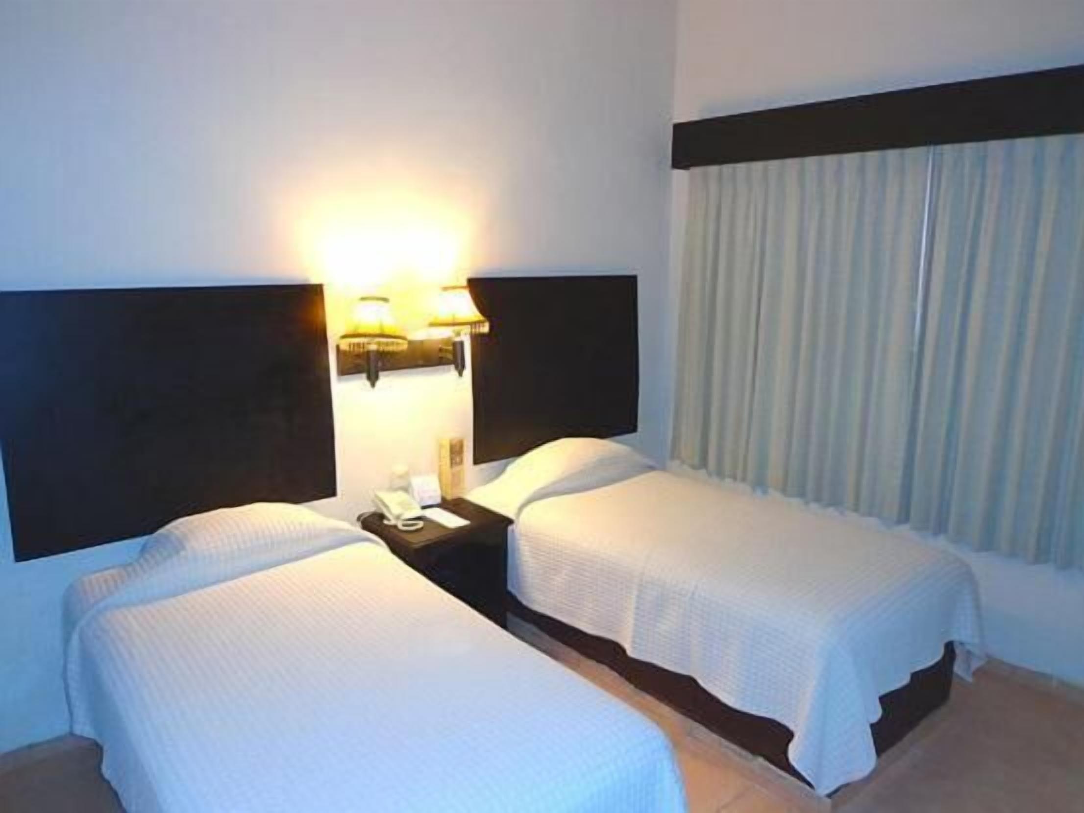 Ein Hotelzimmer mit zwei Betten, einem Nachttisch und einer Lampe.