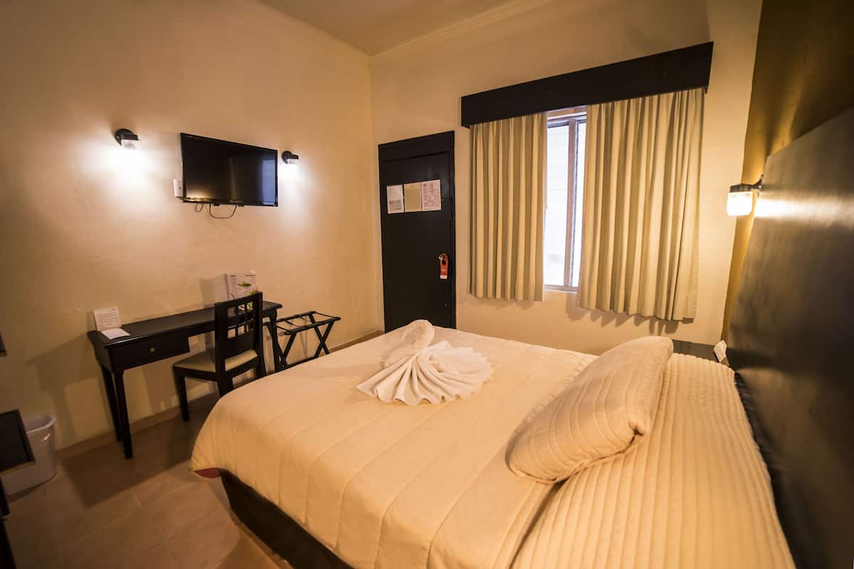 A hotel room with a bed, a desk, a chair, a television, and a window with curtains.