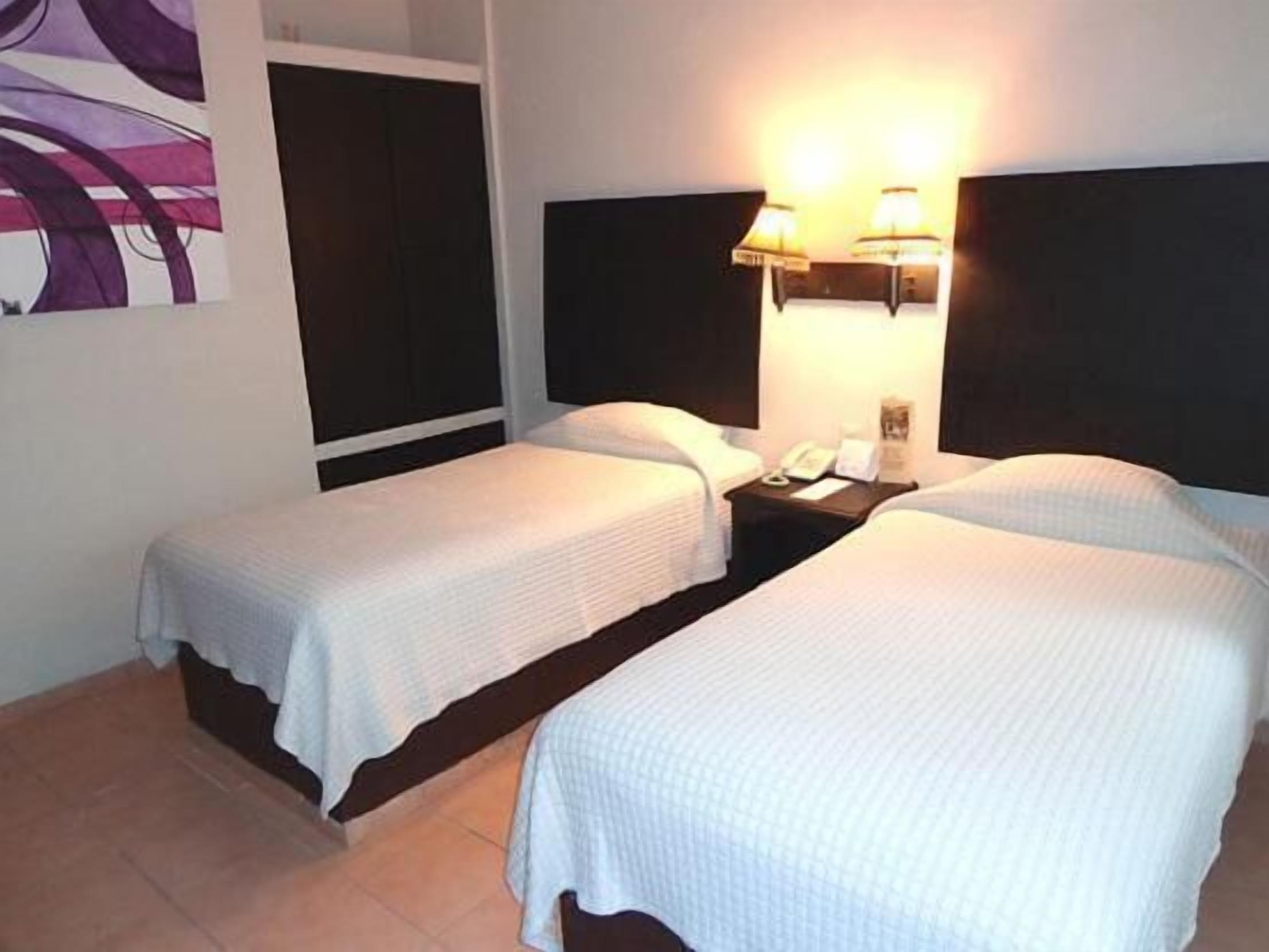Habitación de hotel con dos camas individuales, una mesita de noche con un teléfono y una lámpara, y un cuadro abstracto grande en la pared.