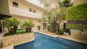 Piscina cercada por plantas em vasos e uma parede verde.