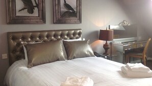 Ein Hotelzimmer mit einem großen Bett, zwei gerahmten Wandbildern, einem Schreibtisch mit Lampe und einem Sessel.